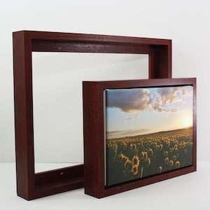 May include: Two dark wood picture frames. One is empty, the other contains a canvas print of a sunflower field at sunset. The frames are rectangular with a deep profile, and the wood has a rich, reddish-brown tone.