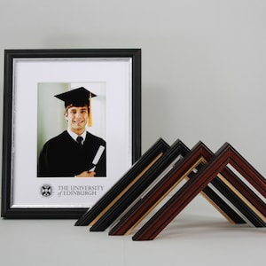 May include: A black picture frame with a silver border and a graduation photo of a person wearing a cap and gown. The frame has the text "The University of Edinburgh" and a logo. Five different picture frames are arranged in a triangular shape in the foreground.