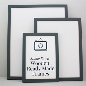 May include: Three grey wooden picture frames of different sizes. The smallest frame has the text "Studio Range Wooden Ready Made Frames" printed on a white background.