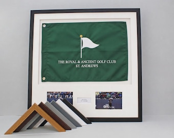 Puede incluir: Una bandera de golf verde enmarcada con un icono de bandera blanca y el texto THE ROYAL & ANCIENT GOLF CLUB ST. ANDREWS. Debajo de la bandera hay dos pequeñas fotografías y una etiqueta. Cinco muestras de esquinas de marco angulares están delante.