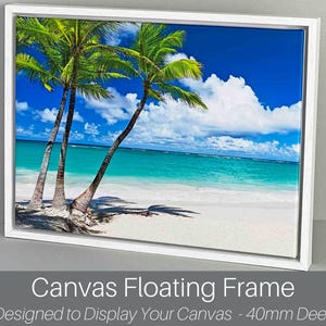 May include: A framed canvas print depicting a tropical beach with palm trees, white sand, and turquoise water under a bright blue sky with white clouds. The canvas is set in a white floating frame.