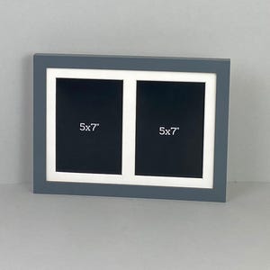 May include: A grey double photo frame with two openings. Each opening has a black background and a white border. The text "5x7" is printed in white on each black background. The frame is designed to hold two 12.7 x 17.8 cm photos.