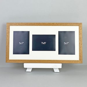 May include: A triple photo frame with a light brown wooden frame and a white mount. The frame holds three photos: two 5x7 inch photos and one 7x5 inch photo. The frame is displayed on a white stand.