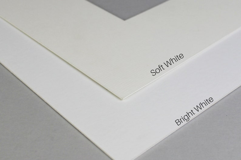 Puede incluir: Primer plano de dos cartulinas blancas, una etiquetada como "Soft White" y la otra como "Bright White". Las cartulinas son texturizadas y muestran una sutil diferencia de color.