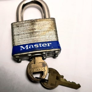 May include: A silver padlock with a blue "Master" label and a brass key with the same branding. The padlock has a worn, aged appearance.