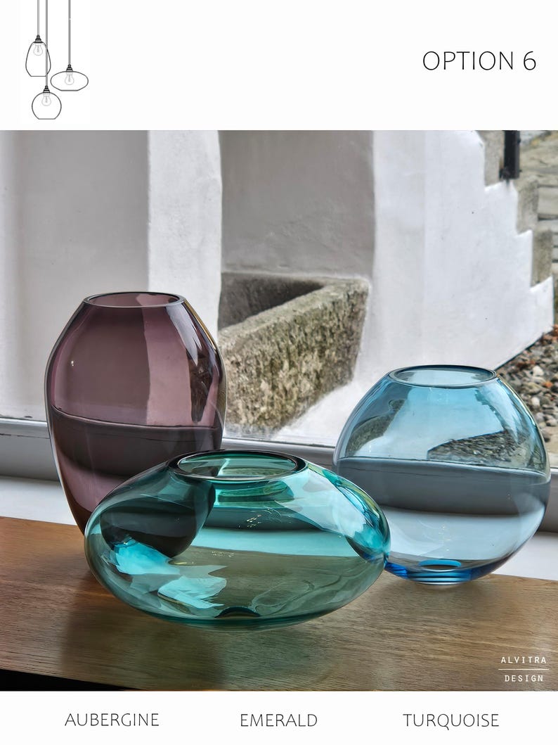 May include: Three glass vases in aubergine, emerald, and turquoise hues. The aubergine vase is tall and rounded, the emerald vase is low and wide, and the turquoise vase is spherical. The vases are displayed on a wooden surface with the text "OPTION 6".