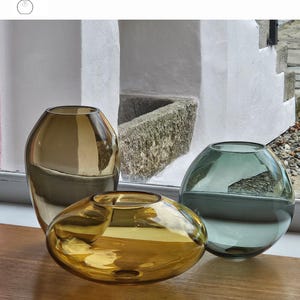 May include: Three glass vases in amber, old gold, and smoke grey hues. The amber vase is oval-shaped, the old gold vase is tall and irregular, and the smoke grey vase is spherical. The vases are displayed on a wooden surface. The text "OPTION 14" is visible.