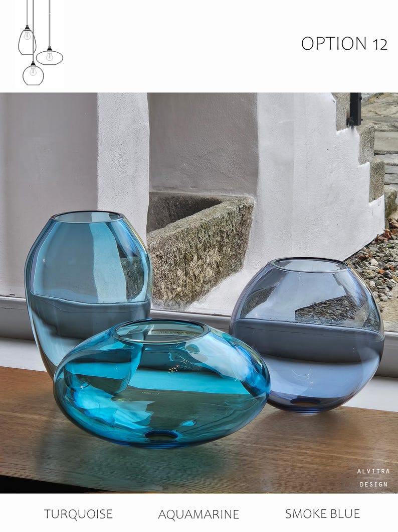 May include: Three glass vases in turquoise, aquamarine, and smoke blue hues. The vases have rounded shapes, with one being a flattened oval. The text "OPTION 12" is visible. The vases are displayed on a wooden surface.