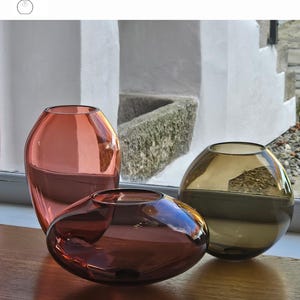 May include: Three decorative glass vases in shades of red, brown, and gold sit on a wooden surface. The vases are labeled "Aurora", "Sangria", and "Old Gold". The image also includes the text "Option 1" and "Alvitra Design".