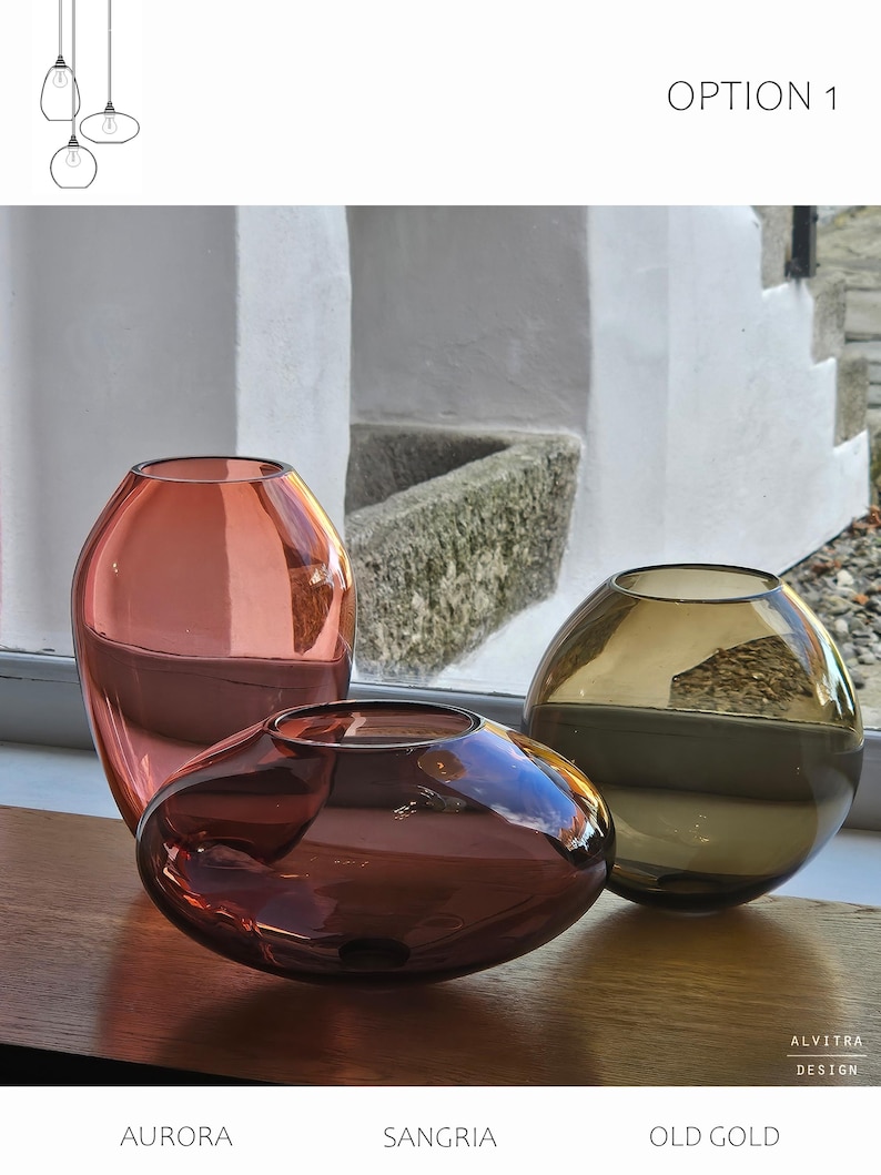 May include: Three decorative glass vases in shades of red, brown, and gold sit on a wooden surface. The vases are labeled "Aurora", "Sangria", and "Old Gold". The image also includes the text "Option 1" and "Alvitra Design".