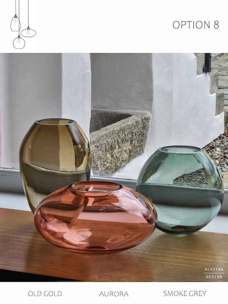 May include: Three glass vases in shades of old gold, aurora, and smoke grey sit on a wooden surface. The vases have unique shapes, including a tall, rounded vase, an oval-shaped vase, and a spherical vase. The text "OPTION 8" is visible.
