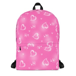May include: Pink backpack with a white heart pattern. The hearts are drawn in a sketchy style and are scattered across the bag.