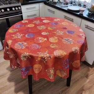 Könnte beinhalten: Runder roter Tischläufer mit einem Weihnachtsbaumschmuckmuster. Der Tischläufer hat eine goldene Glitzer-Oberfläche und zeigt eine Vielzahl von bunten Ornamenten.