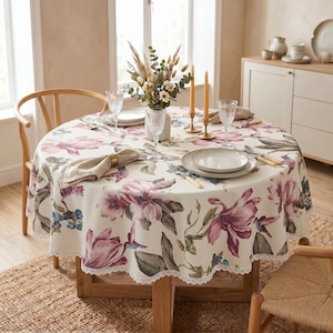 May include: A round tablecloth with a floral pattern in shades of pink, purple, and blue, set on a wooden table. The table is set with plates, glasses, and silverware, with a vase of flowers and candles.