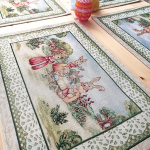 May include: Four green and white embroidered placemats with a bunny rabbit theme. The placemats feature a white lace border and a checkered pattern. The center of each placemat features a different scene with bunnies, flowers, and eggs.