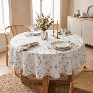 May include: A round wooden table set for a meal, featuring a white tablecloth with a gray leaf pattern. The table is set with plates, silverware, and wine glasses. A vase of flowers and candles add to the decor. The table is approximately 48 inches in diameter.