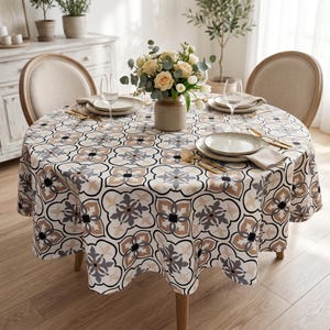 May include: A round dining table set for a meal, featuring a patterned tablecloth with a floral design in beige, gray, and black. The table is set with plates, silverware, and a vase of flowers. Two chairs are visible.