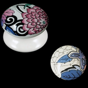 May include: Two white ceramic knobs with floral designs. The top knob has a pink and blue floral design. The bottom knob has a blue and white floral design.