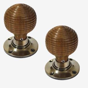 May include: Two wooden door knobs with a spherical design. The knobs are a warm brown colour and feature a grooved texture. They are mounted on round, brass-coloured plates with screw holes, suitable for interior doors.