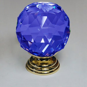 May include: A blue crystal door knob with a gold base. The crystal is faceted and has a shiny finish.