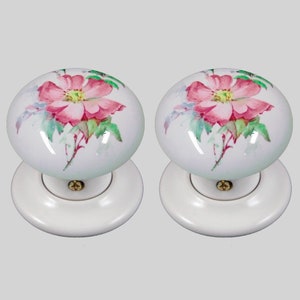 May include: Pair of white ceramic door knobs with a pink rose floral design.