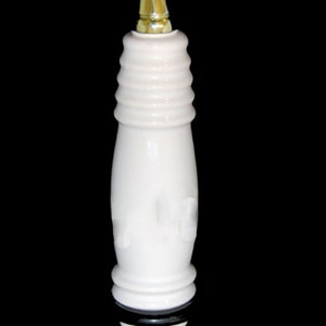 May include: White ceramic bottle stopper with a gold top. The stopper has a ribbed design and a black rubber ring around the base.