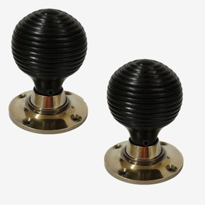 Può includere: Coppia di pomelli per porte neri con basi in ottone. I pomelli hanno un design a coste.