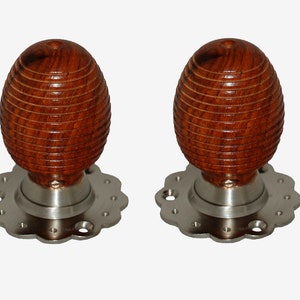 Può includere: Due pomelli per porte in legno con un design marrone scuro, scanalato, a forma di uovo. I pomelli sono montati su una base argentata smerlata. L'hardware è progettato per porte interne.