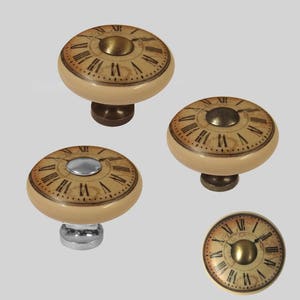 Puede incluir: Cuatro pomos de armario de cerámica con un diseño de esfera de reloj. Los pomos tienen un fondo beige con números romanos marrones y un centro dorado. Los pomos tienen bases de diferentes colores: oro, plata y bronce.