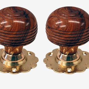 Può includere: Due pomelli per porte in legno con finiture in ottone e bordo smerlato. I pomelli sono di colore marrone scuro con una venatura del legno.