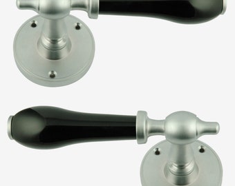Könnte beinhalten: Zwei schwarze Keramik-Türgriffe mit silbernen Metallsockeln. Die Griffe haben eine abgerundete, längliche Form.