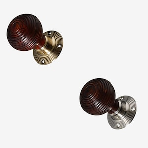 Könnte beinhalten: Zwei Türknauf mit dunklem Holzfinish und einem runden, gerillten Design. Ein Knauf hat eine Messing-Grundplatte und der andere eine Nickel-Grundplatte.