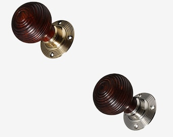 Op de afbeelding: Twee deurknopjes met een donkerhouten afwerking en een rond, gegroefd ontwerp. Eén knop heeft een messing basisplaat en de andere een nikkel basisplaat.