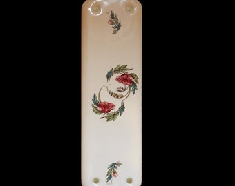 Op de afbeelding: Witte keramische deurknop-afdekking met een bloemenontwerp met rode en groene bloemen. De afdekking heeft twee gaten voor montage.