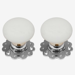May include: Two white ceramic door knobs with a chrome base and a decorative scalloped edge.
