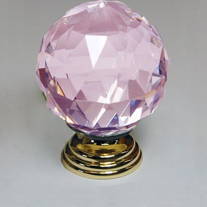 May include: A pink crystal door knob with a gold base. The crystal is faceted and has a round shape.