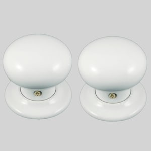 May include: Two white ceramic door knobs with a round shape and a flat base. The knobs have a small gold screw in the center.