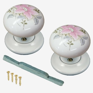 May include: A pair of white ceramic door knobs with a pink floral design. The knobs come with a silver metal door handle and four gold screws.