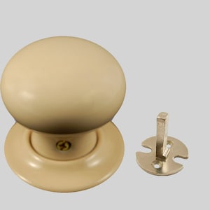 May include: A cream-colored door knob with a round shape and a flat base. The knob has a small screw in the center. The knob is shown with a separate metal mounting plate.