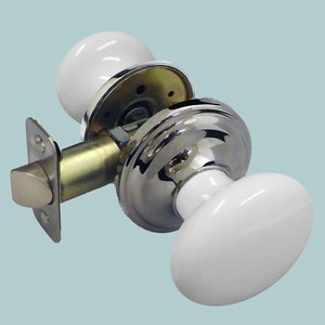 May include: A white porcelain door knob set with a polished chrome base and a brass-coloured latch plate. The oval-shaped knobs are smooth and glossy, offering a classic design for interior doors.