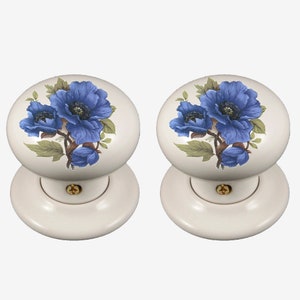 May include: Two white ceramic door knobs with blue floral designs. Each knob features a cluster of blue flowers with green leaves.