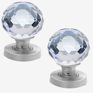 Peut inclure: Deux boutons de porte en cristal avec un design facetté et une base argentée. Les boutons sont ronds et ont une finition brillante.