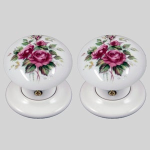 May include: Two white ceramic door knobs with a floral design featuring pink roses and green leaves.