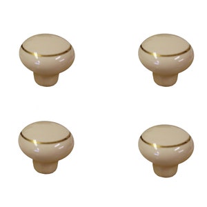 May include: Set of four off-white ceramic cabinet knobs with a gold trim. Each knob has a rounded top and a short, cylindrical base.