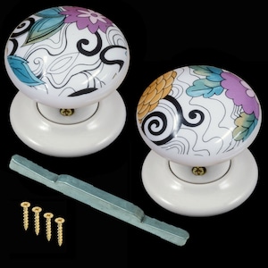 Può includere: Due pomelli per porte in ceramica bianca con un design floreale e a spirale in tonalità di blu, giallo, rosa e nero. I pomelli sono fissati su basi bianche e vengono forniti con una maniglia per porta in metallo argentato e viti.