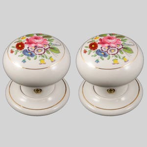 May include: Pair of white ceramic door knobs with a gold trim and a floral design. The floral design features pink, red, yellow, blue, and green flowers.