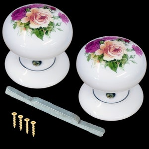May include: Two white ceramic door knobs with floral designs. The knobs feature pink and yellow roses with green leaves. The knobs are shown with a silver metal latch and four gold screws.