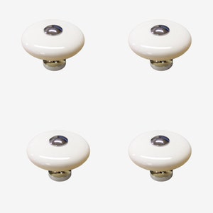 May include: Set of four white ceramic cabinet knobs with a silver metal accent. Each knob has a round, flat top and a small, round, silver metal knob in the centre.