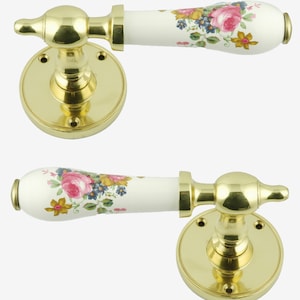 Pode incluir: Duas maçanetas com acabamento dourado e puxadores de porcelana branca. Os puxadores de porcelana são decorados com um padrão floral em rosa, amarelo e azul. As maçanetas são montadas em placas redondas douradas.