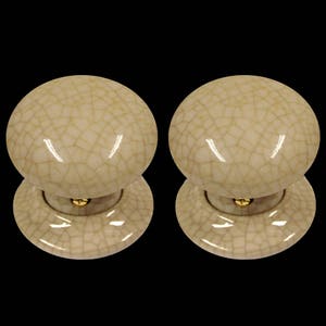 Könnte beinhalten: Zwei Keramik-Türknäufe mit einer craquelé-Glasur. Die Knäufe sind hellbeige mit einem goldenen Akzent.